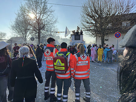 auf dem Foto sind drei ehrenamtliche Einsatzkräfte zu sehen, die Sanitätswachdienst bei einem Fastnachtsumzug leisten.