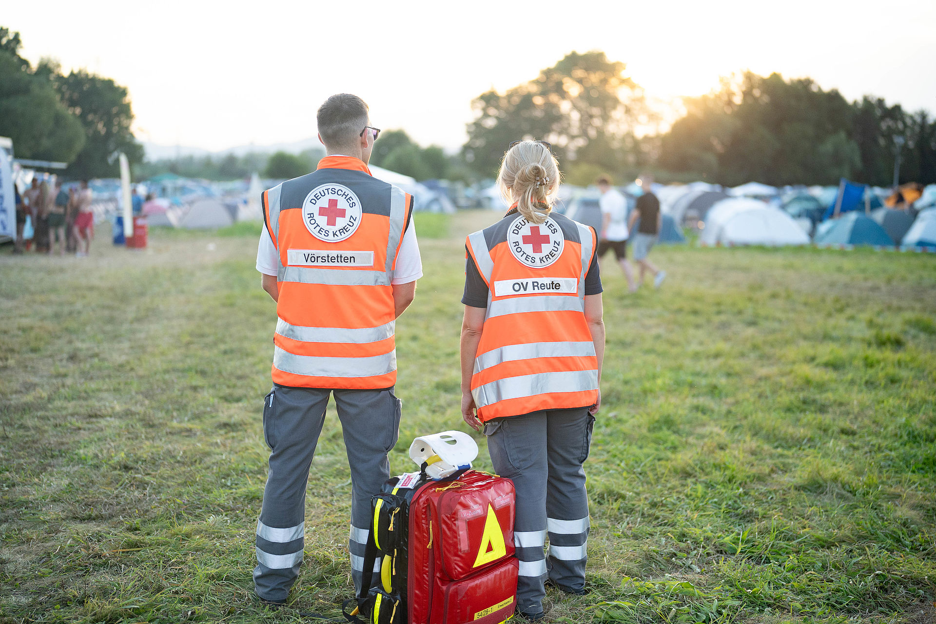 Zwei Einsatzkräfte beim Sanitätsdienst bei einem Festival. Im Hintergrund ist eine Zeltstadt zu sehen.